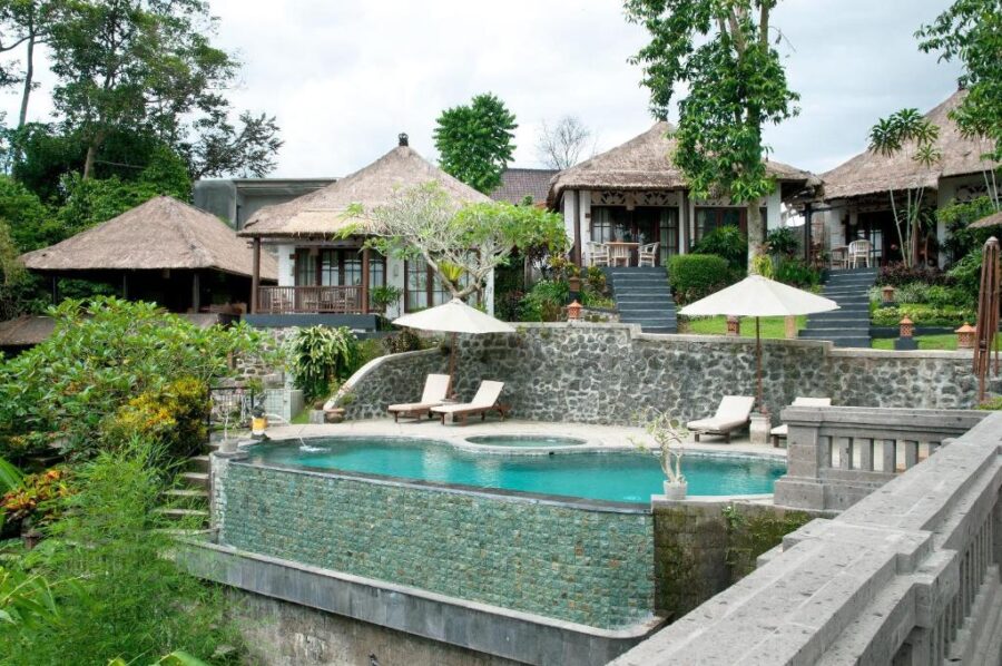 Luxury tropical hillside resort with infinity pool, thatched villas, lush jungle views, and sun loungers.