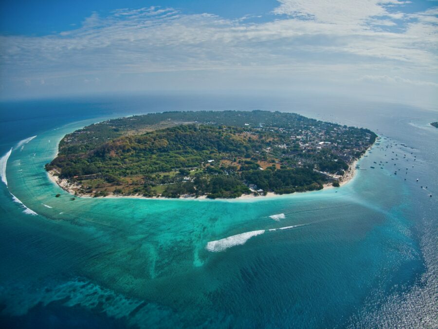 Aerial view of tropical island with coral reef, turquoise lagoon, white sand beach, and village.