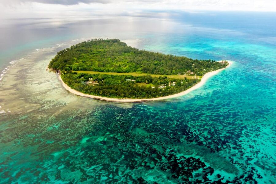 Aerial view of small tropical Seychelles island with white sandy beach, lush palm forest and turquoise lagoon.