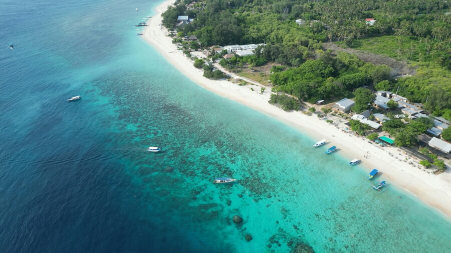 Aerial view of tropical beach coastline with turquoise water, boats, white sand, and lush greenery.