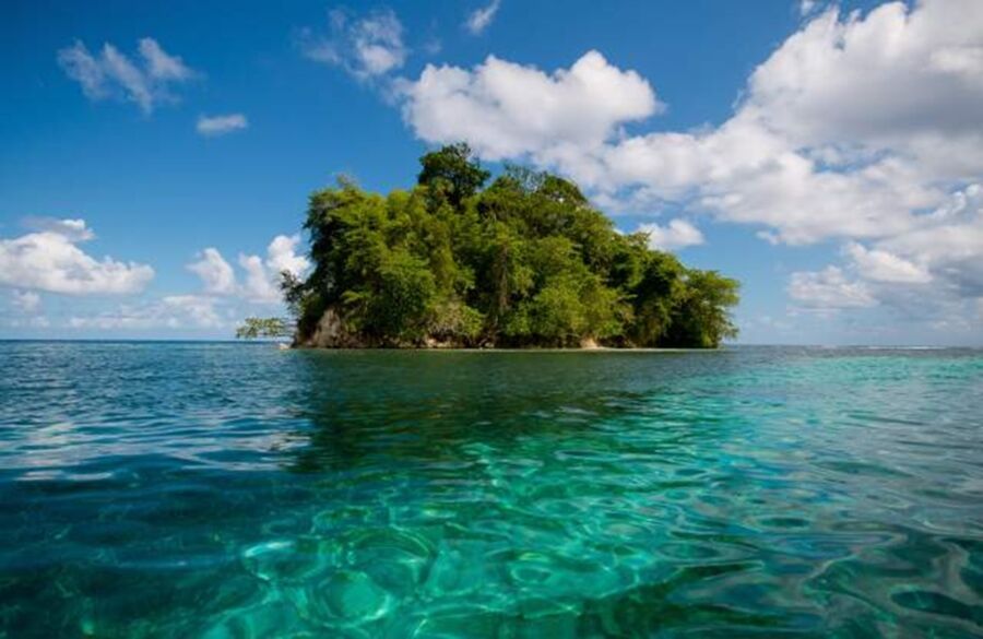 Tropical island with lush greenery, turquoise waters, and serene skies.