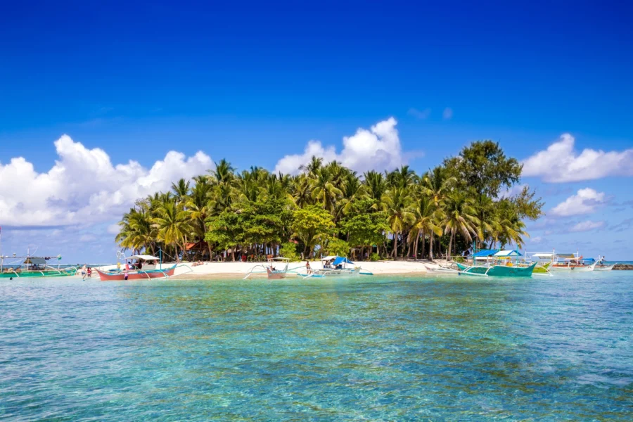Siargao islet with white sand, coconut palms, turquoise water, and colorful outrigger boats.
