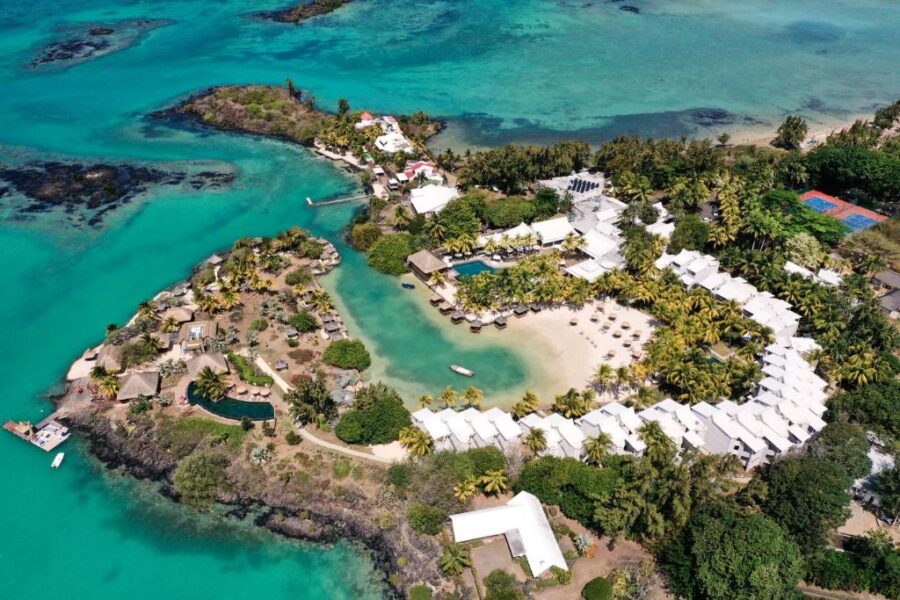 Aerial view of tropical lagoon beachfront resort with overwater villas, pools, palm trees, and turquoise sea.