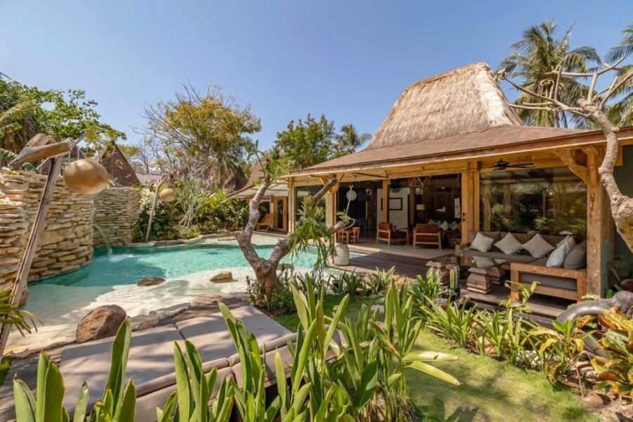 Luxury tropical villa with lagoon-style pool, lush garden, palm trees, and open-air living area.