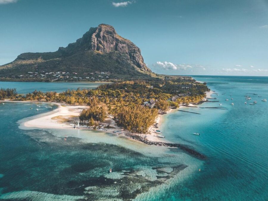 Tropical lagoon beach with white sand, turquoise water and lush mountain on Mauritius coastline.