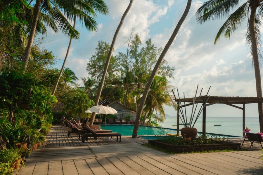 Serene tropical resort with palm trees, pool, sun loungers, and villa at sunset.
