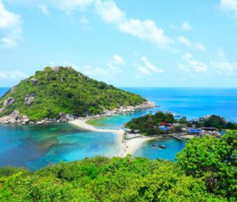 Tropical Koh Samui island with lush greenery, sandy beach, fishing village, and historic structures in azure waters.