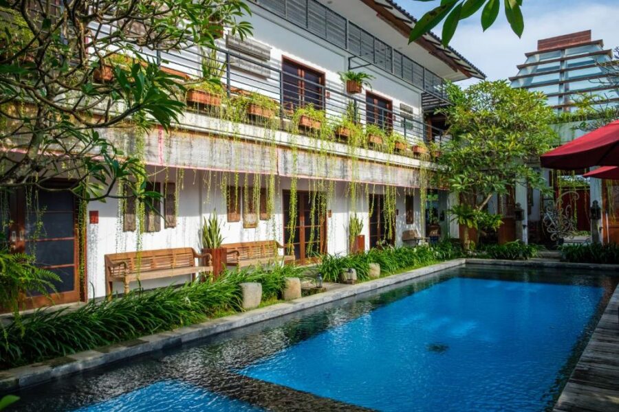 Tropical boutique hotel courtyard with swimming pool, lush greenery, balcony rooms, and relaxing poolside deck.