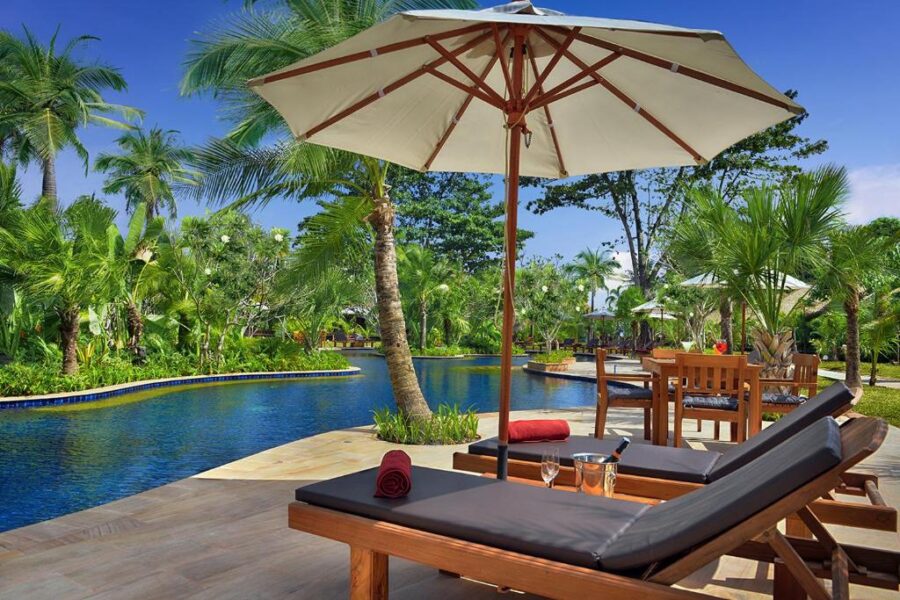 Luxury tropical resort pool with lounge chairs, umbrellas, palm trees, and relaxing oceanfront vacation vibes.