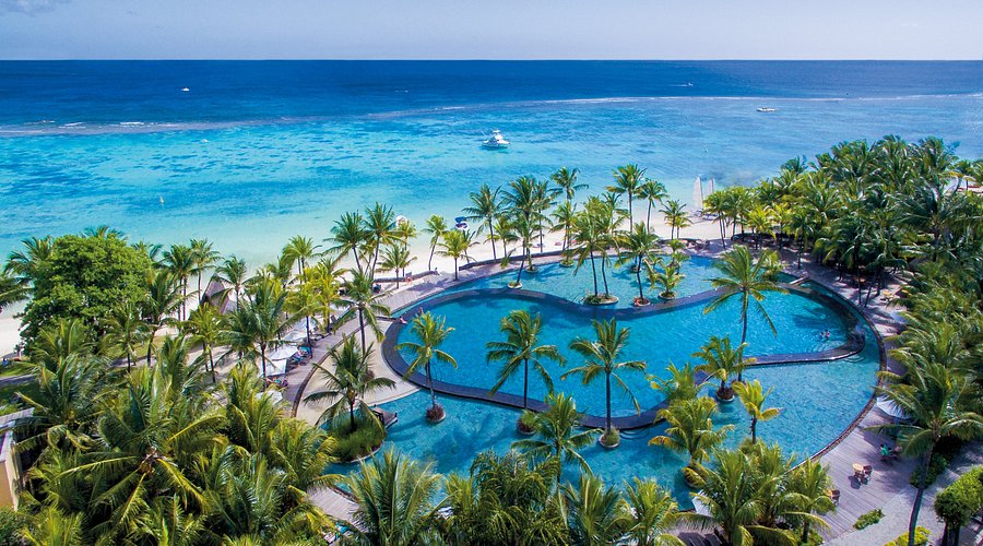 Luxury tropical beachfront resort with infinity pool, palm trees, white sand beach, and turquoise ocean.