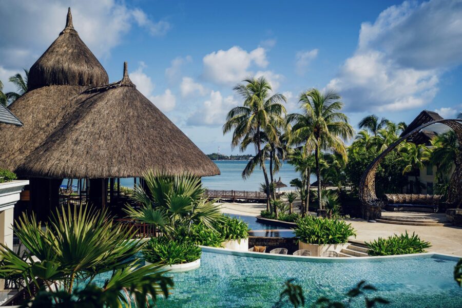 Luxury tropical resort infinity pool with palm trees, thatched roofs, ocean view, serene vacation.