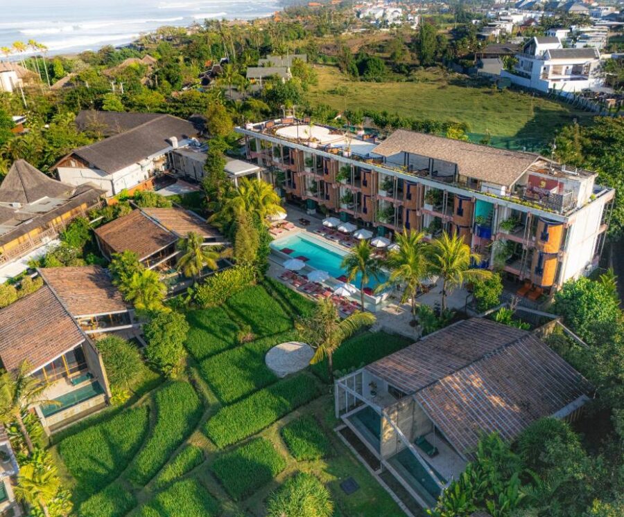 Luxury tropical resort with infinity pool, rice fields, palm trees, and ocean coastline aerial view.
