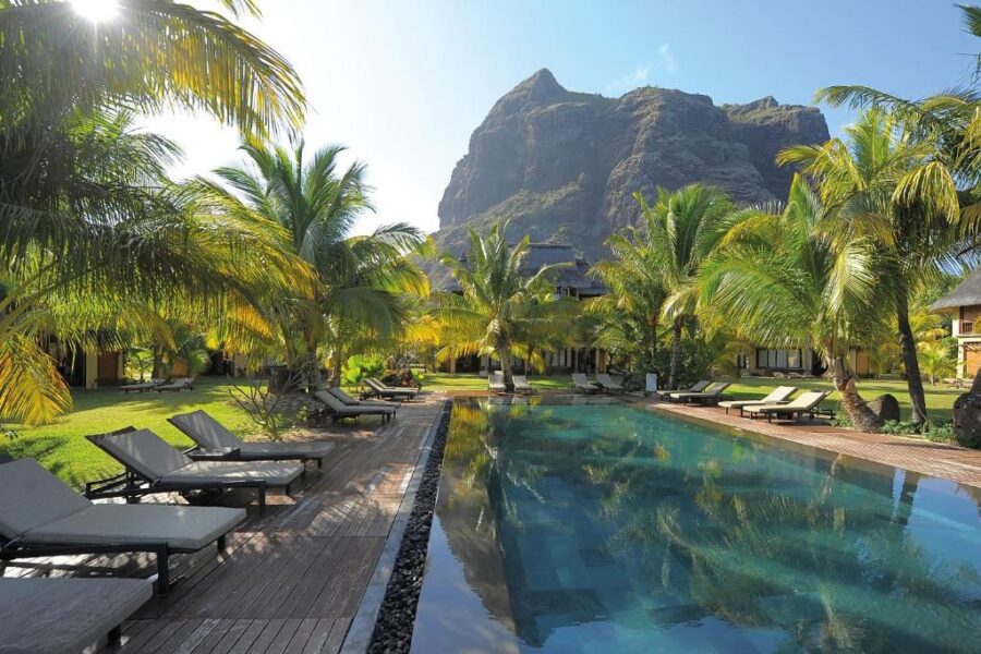 Luxury tropical resort pool with palm trees, mountain backdrop, sun loungers, and serene vacation setting.