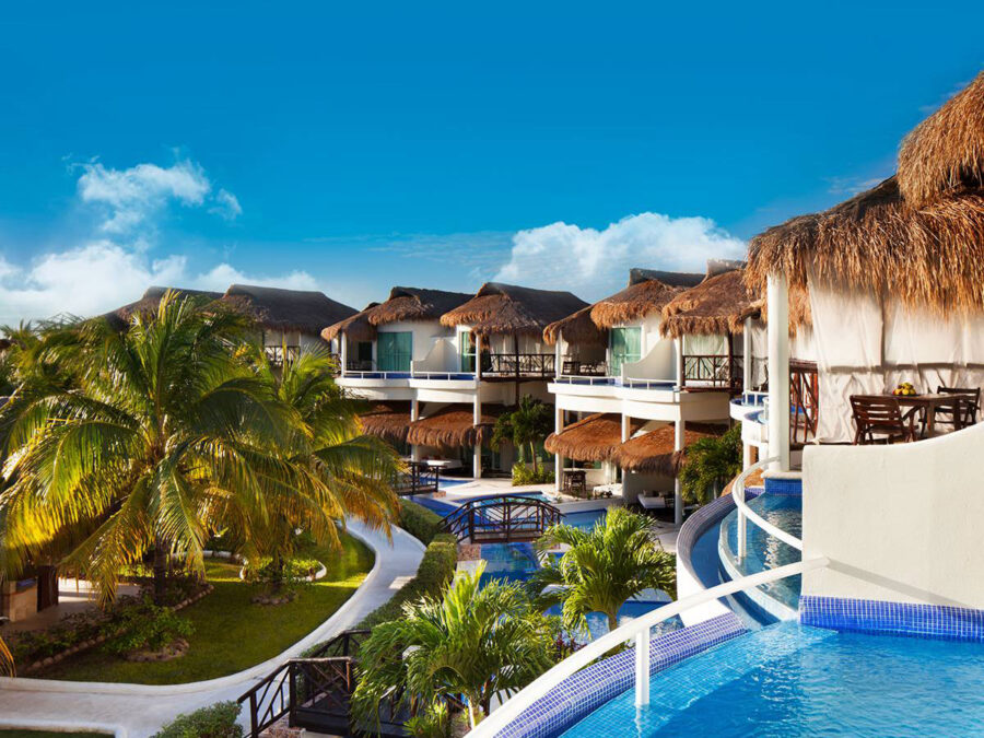 Luxurious tropical resort with thatched roofs, winding pools, palm trees, and lush greenery.