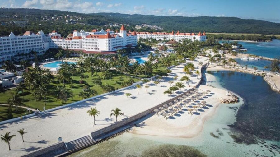 Luxurious beachfront resort with orange roofs, sandy beach, palm trees, and turquoise waters.