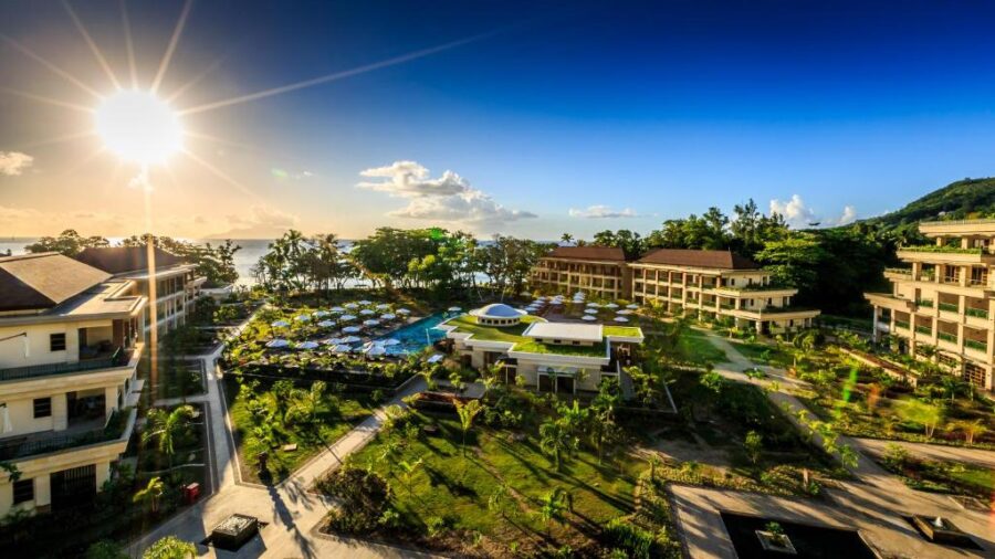 Luxury Seychelles beach resort with tropical gardens, oceanview pool, sun loungers and sunset sky.