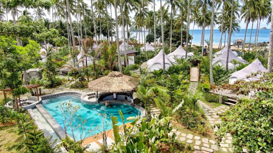 El Nido glamping resort with turquoise pool, beachfront bungalows, and palm trees.