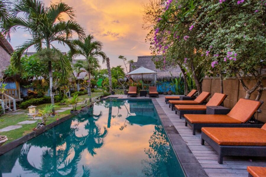 Luxury tropical resort pool at sunset with palm trees, lounge chairs, bougainvillea and cabanas.