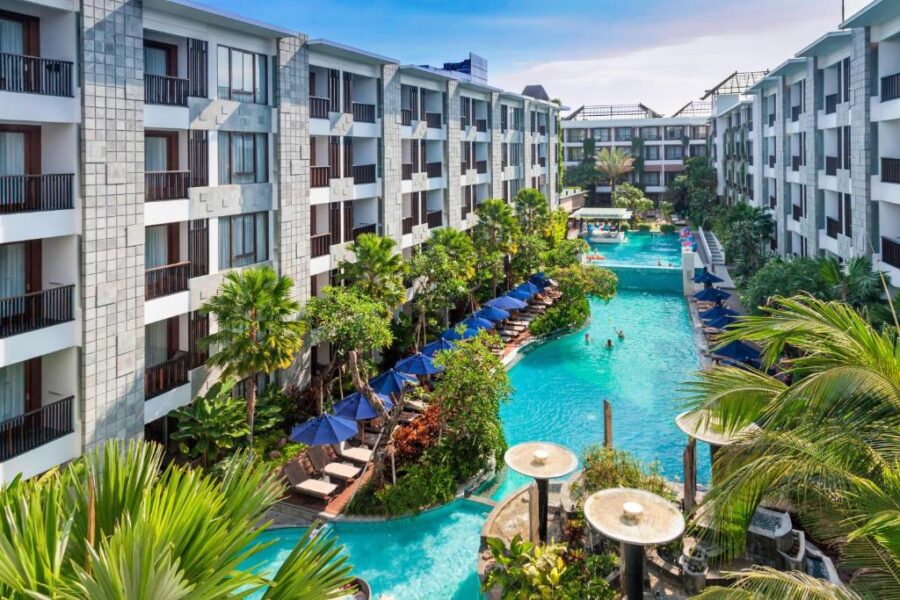 Luxury Bali resort lagoon pool with tropical palm trees, loungers, umbrellas and modern suites.