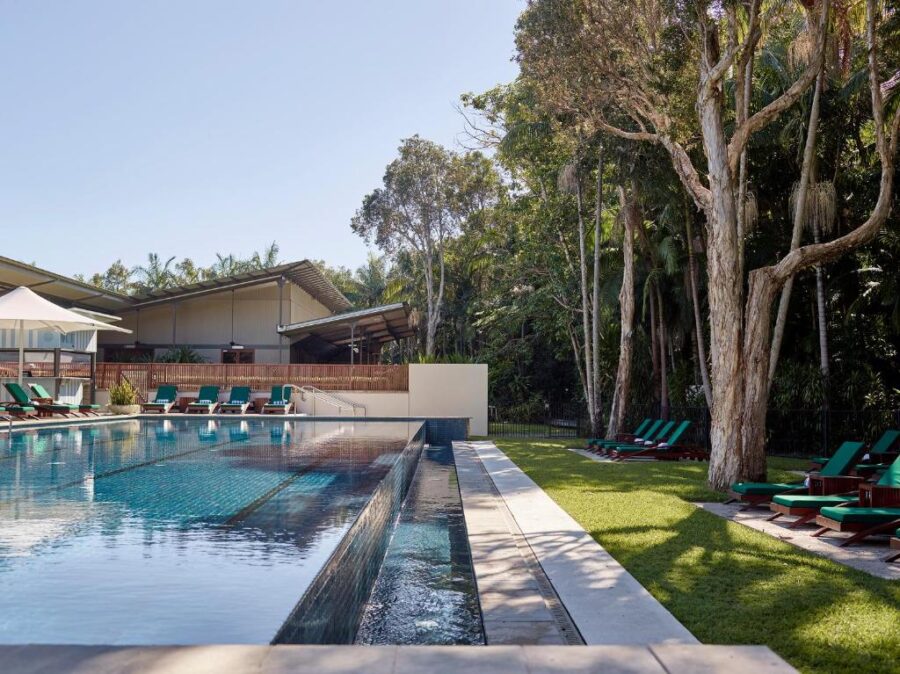 Luxury tropical resort swimming pool with lounge chairs, rainforest trees, and tranquil Byron Bay setting.