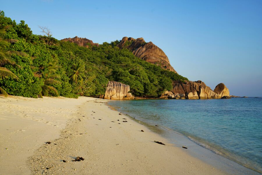 Secluded tropical beach with granite rock formations, palm trees, white sand, and turquoise ocean water.