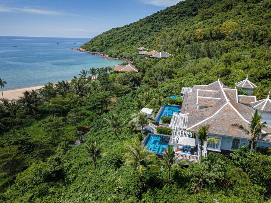 Luxury tropical beach resort with hillside villas, infinity pools, palm trees, and secluded turquoise bay.