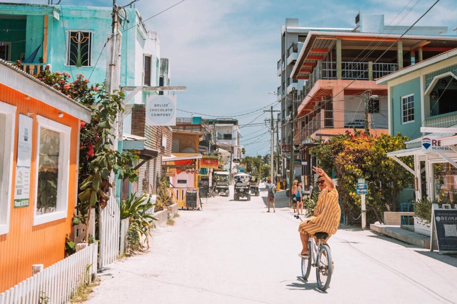 Vibrant coastal street with colorful buildings, cyclist, and Belize Chocolate Company.