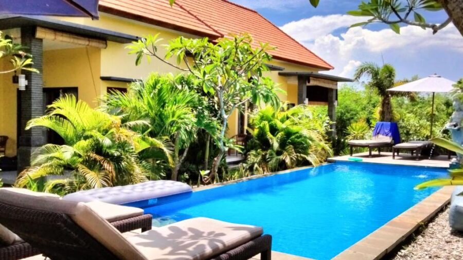 Tropical villa pool retreat with lounge chairs, palm trees, blue sky and luxury vacation vibes.