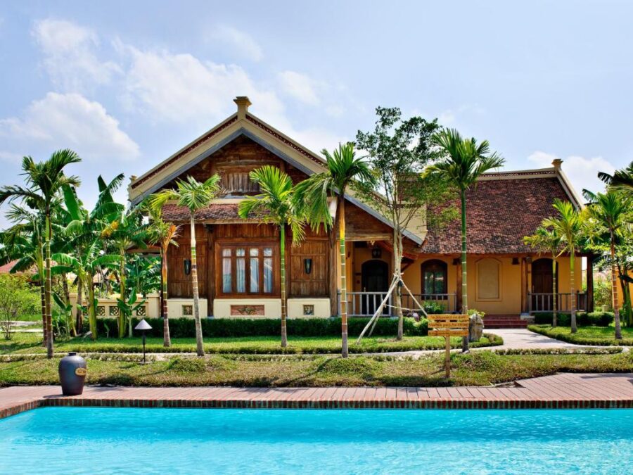 Tropical villa with swimming pool, lush garden, palm trees and traditional tiled roof resort house.