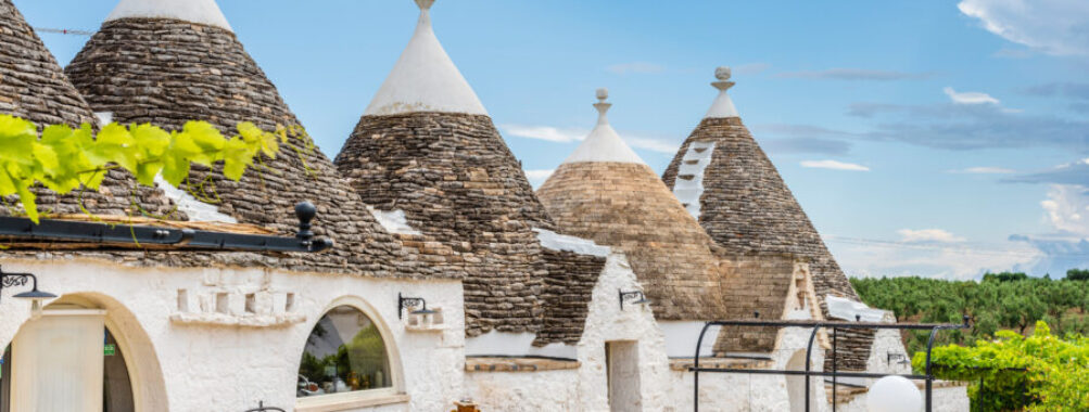 Scenic view of trulli in the Itria Valley with a clear sky, highlighting the traditional structures of Alberobello, Puglia.