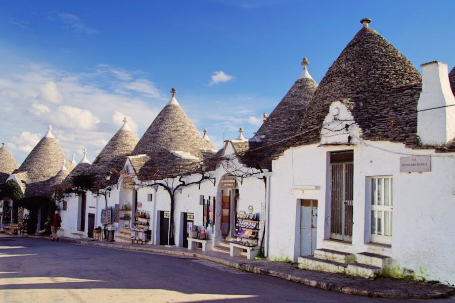 Charming trulli street in Apulia, Italy with blue sky, stone roofs, and local shops.