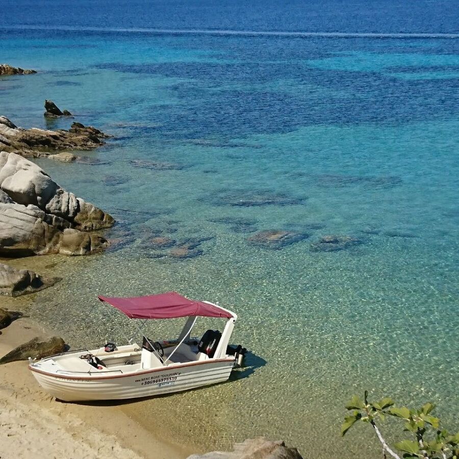 Boat is docked on the sandy beach of Trypiti, Greece, with gentle waves lapping at the shore.