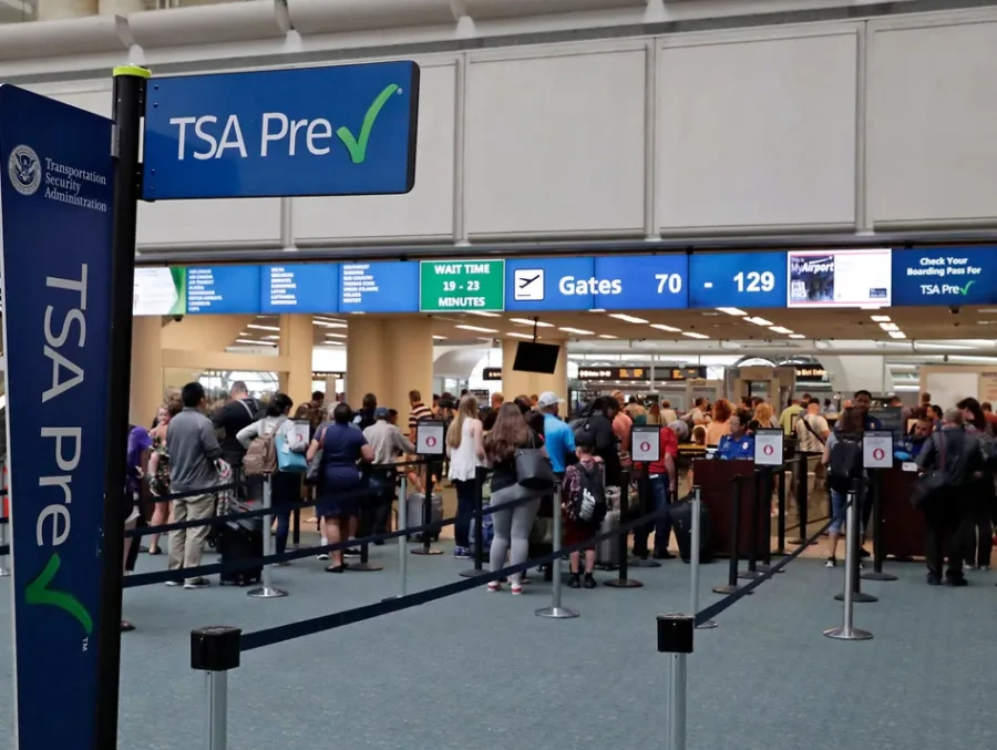 Busy airport terminal with TSA PreCheck sign and travelers waiting in line for security screening.