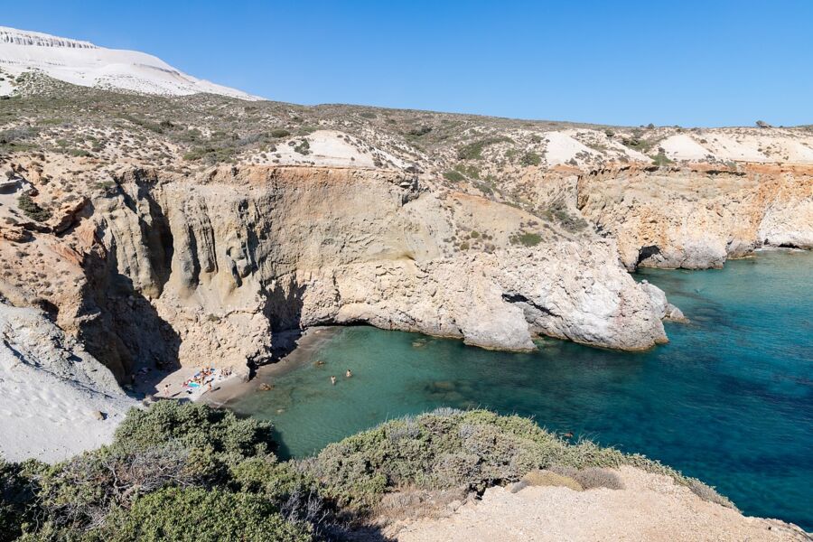 Scenic view of Tsigrado Beach, Milos Island, featuring a cliff, blue ocean, and a few people enjoying the landscape.