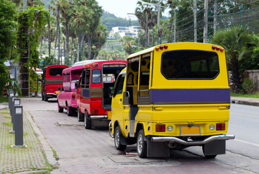 Several brightly painted Tuk tuks lined up in a park in Phuket, Thailand, highlighting the unique local transport