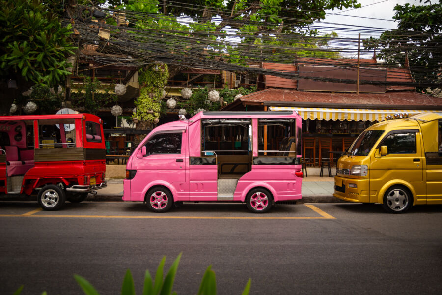 Colorful Tuk tuks lined up in a park in Phuket, Thailand, featuring a variety of hues and unique patterns