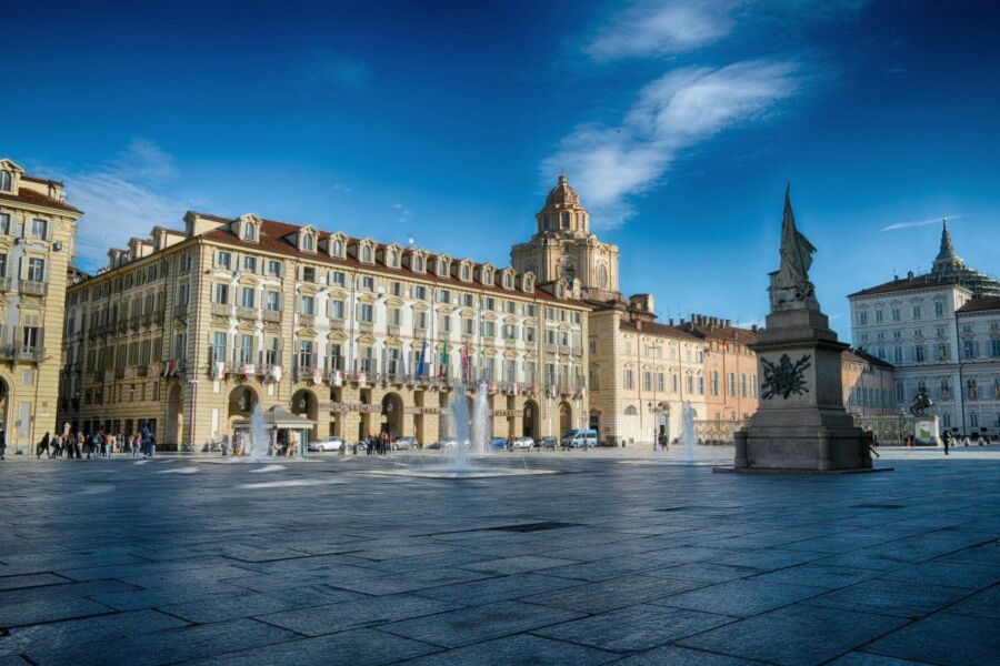 Vibrant Italian city square with baroque architecture, fountains, and crowds under a bright blue sky.