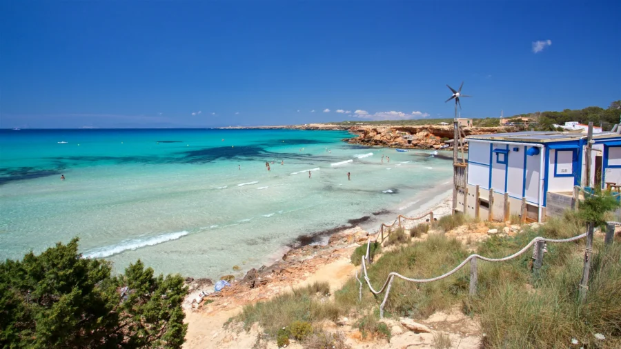 Turquoise Cala Saona beach with sandy coastal path and white beach huts.