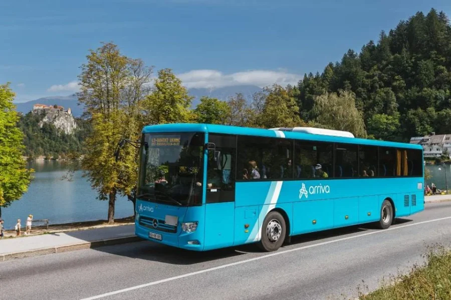 Turquoise Arriva coach traveling from Ljubljana to Bled past Lake Bled castle.