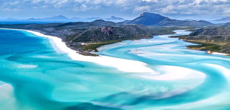 Aerial view of Whitehaven Beach turquoise water, white sandbars, tropical coastline and lush green mountains.