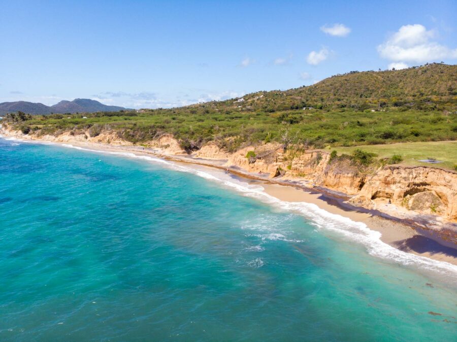 Aerial view of Vieques coastline with turquoise ocean, sandy beach, golden cliffs and green hills.