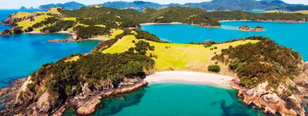Aerial view of turquoise secluded bay, sandy beach and lush green coastal cliffs.