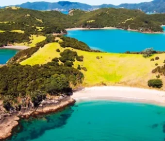 Aerial view of turquoise secluded bay, sandy beach and lush green coastal cliffs.