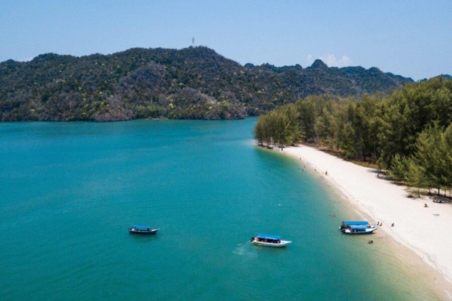 Serene tropical Tanjung Rhu beach with turquoise waters, lush greenery, and anchored boats against hill backdrop.