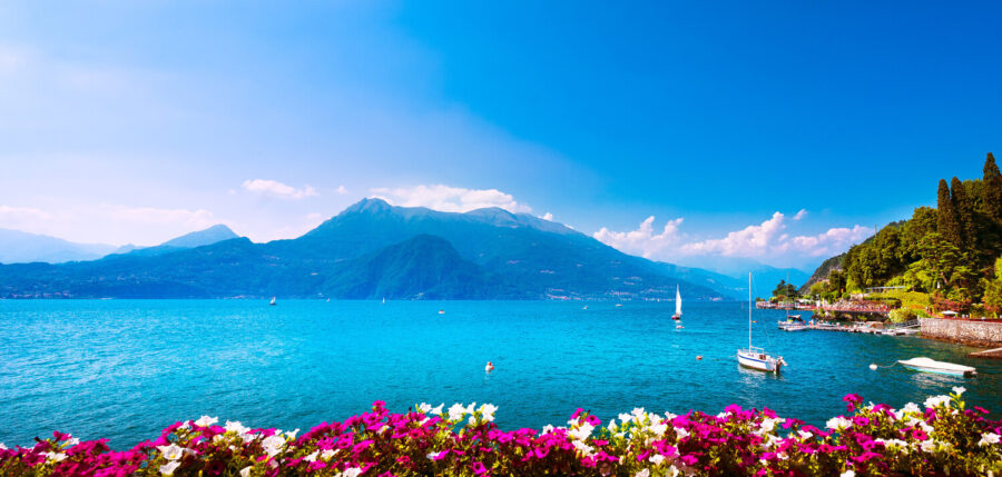 Lake Como, Italy: turquoise water with sailboats, lakeside flowers and Alpine mountains.