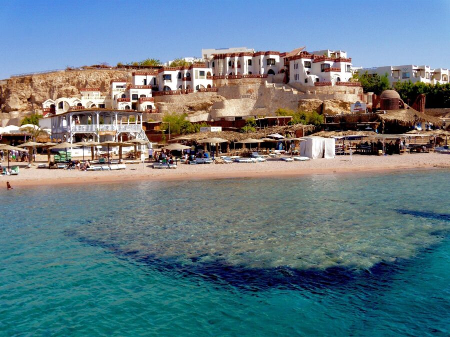 Turquoise Red Sea beach resort at Sharm El Sheikh with cliffside hotels, sun loungers, and umbrellas.