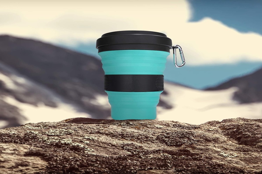 Teal silicone collapsible coffee cup on rock with mountains; portable and eco-friendly travel accessory.