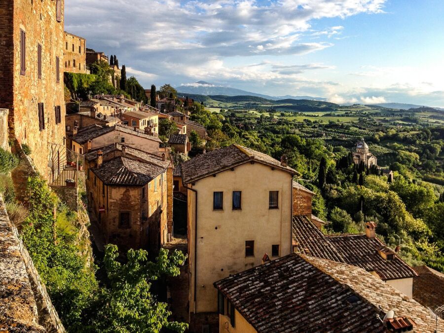Picturesque Tuscan village with rustic houses, cypress trees, rolling hills, and a stunning sunset.