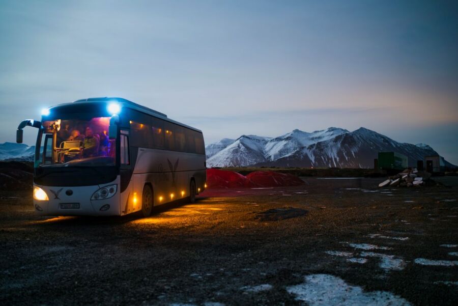 Modern bus parked at dusk, surrounded by snowy mountains and rugged terrain, evoking adventure.