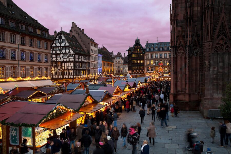Strasbourg Christmas market at twilight with festive wooden stalls and cathedral backdrop.